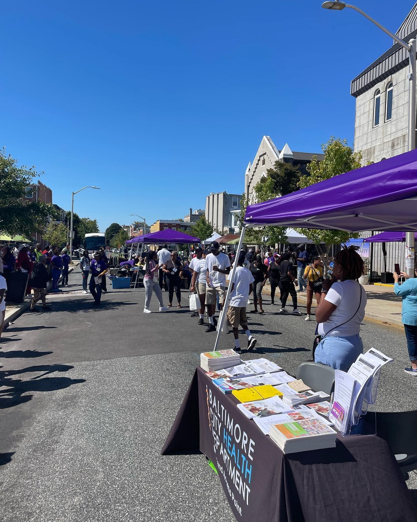 A group of people are standing under purple tents on a street.