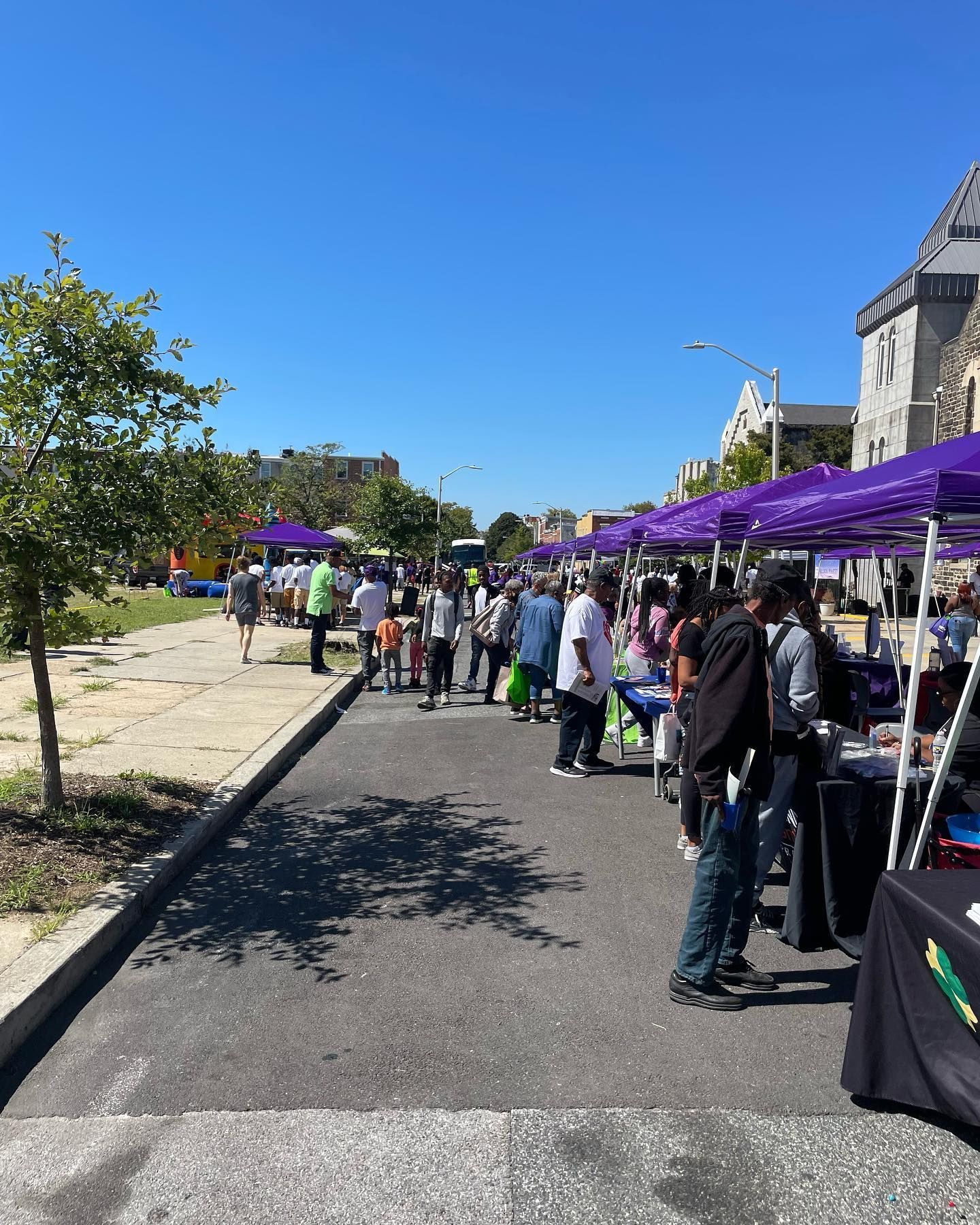 A group of people are standing under purple tents in a parking lot.