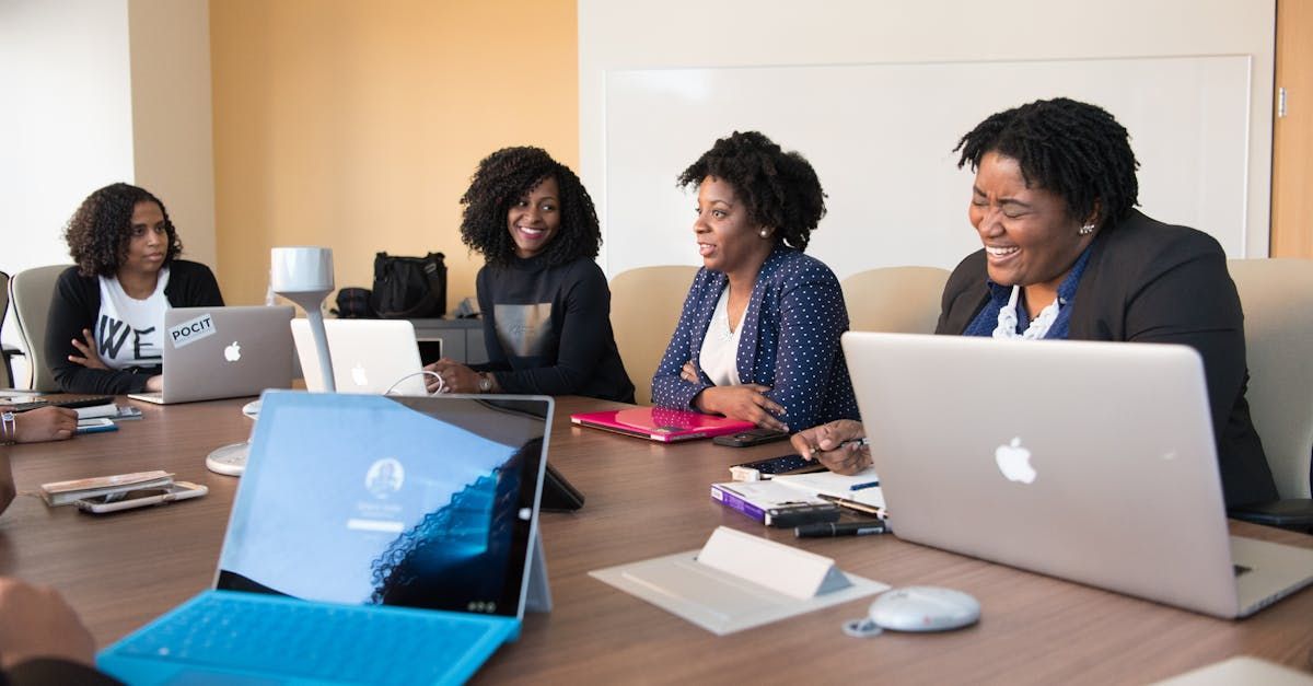 A group of women are sitting at a table with laptops.