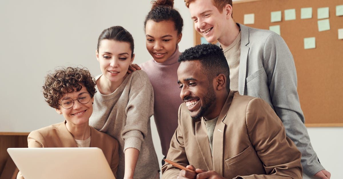A group of people are standing around a laptop computer.