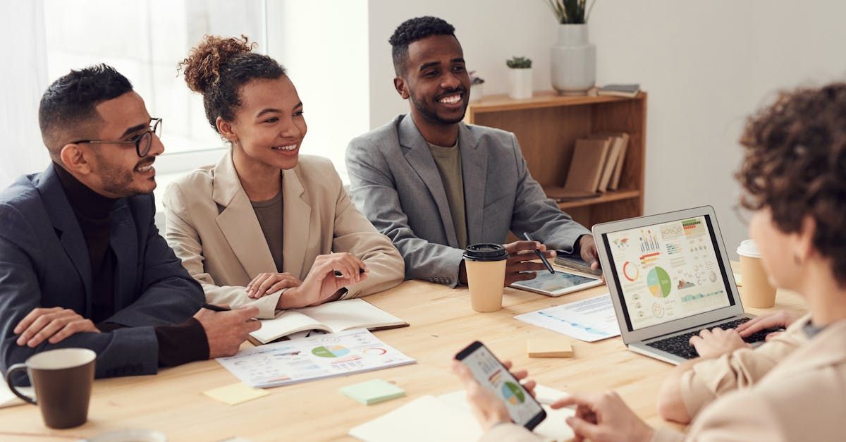 People in business attire at a table, looking at a laptop and smiling.