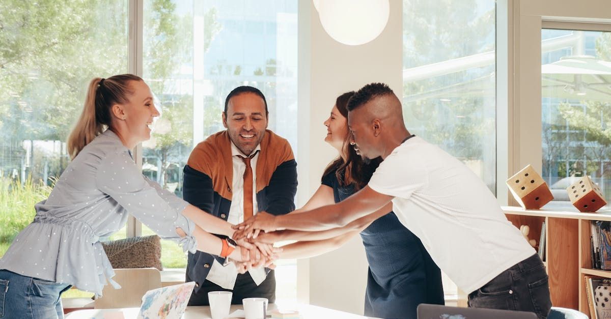 People in a light-filled office, hands stacked together. Cheerful expressions.