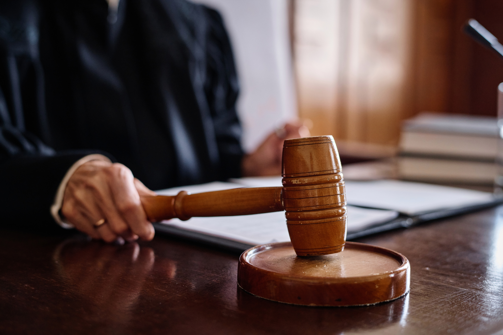 Judge holding a gavel on a wooden desk with documents and books; court setting.