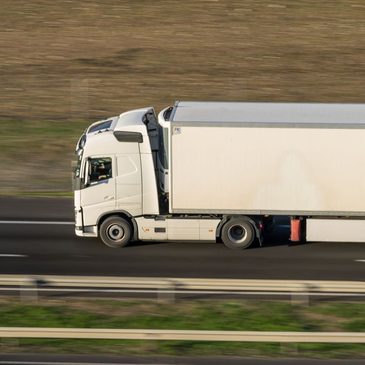 White semi-truck driving on a highway, with a white trailer.