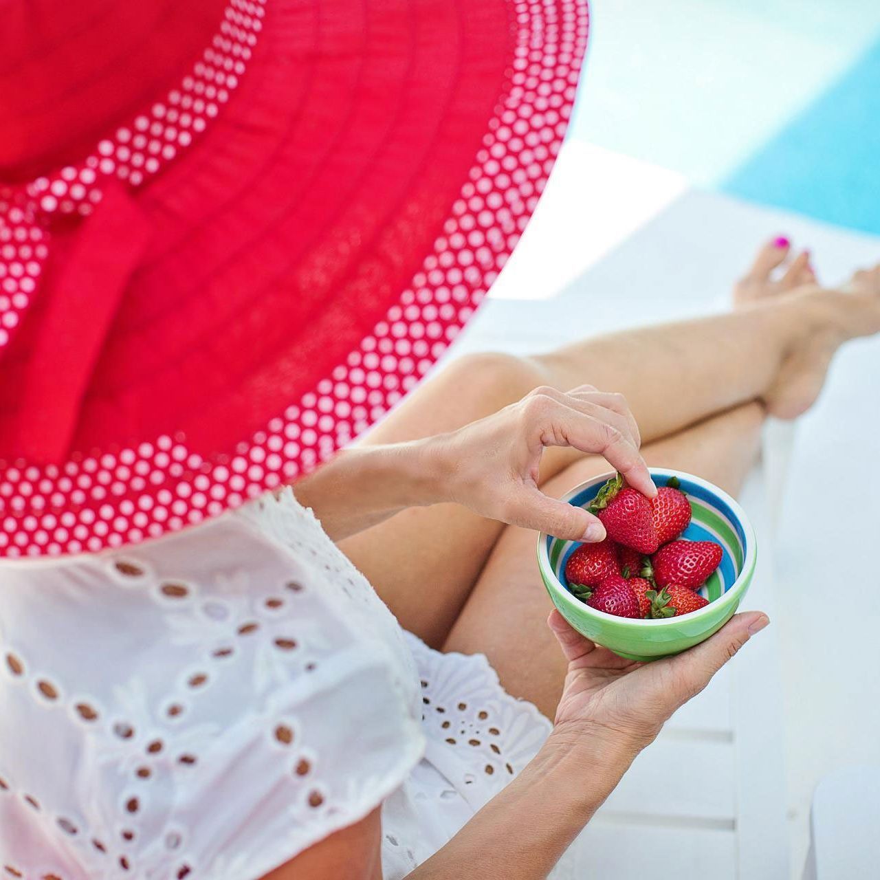 A woman wearing a red hat is holding a bowl of strawberries