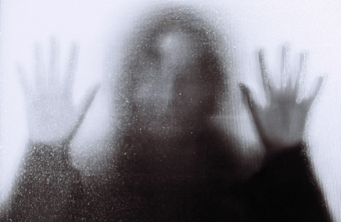 blurred image of a child with their hands pressed against an opaque glass screen