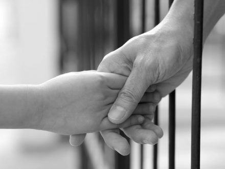 an adult hand grasping a child's hand through prison bars - Photo: iStock
