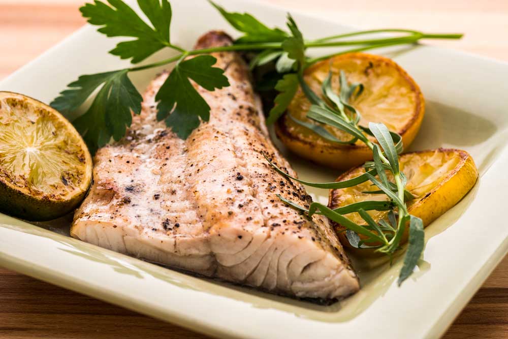 A freshly Grilled and Smoked Walleye plated on a green square plate with herb garnishes and a charred lemon