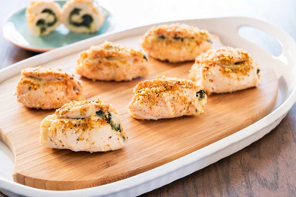A tray of stuffed chicken breasts on a wooden cutting board.
