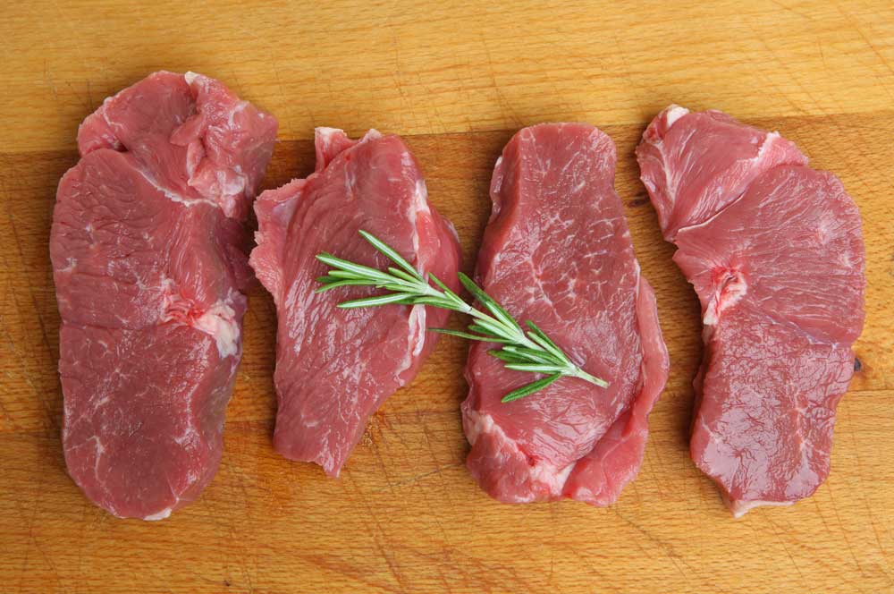 Boneless lamb leg steaks on wooden chopping board