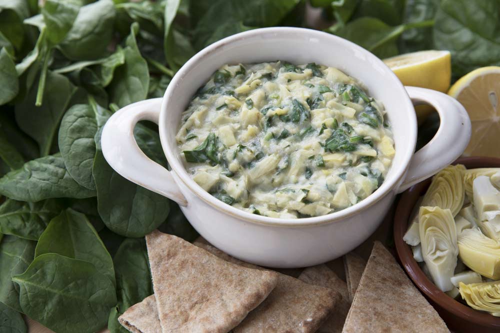 Bowl of vegan spinach artichoke dip with pita and ingredients