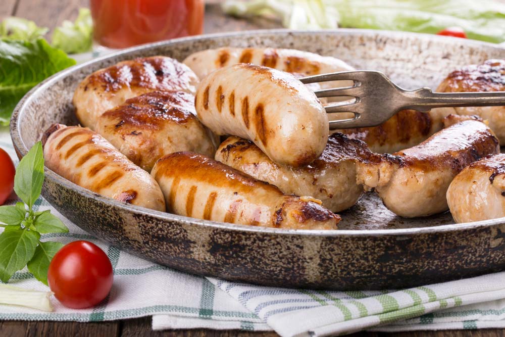 A pan filled with grilled sausages with a fork in it.