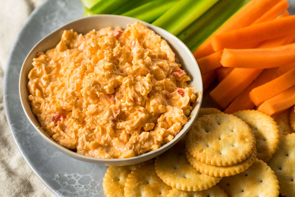A bowl of dip next to crackers and carrots on a plate.