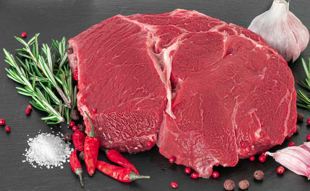 Raw beef steak with spices on a dark board