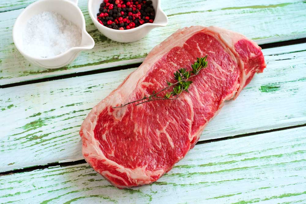 Raw strip loin steak on white wooden background in rustic style