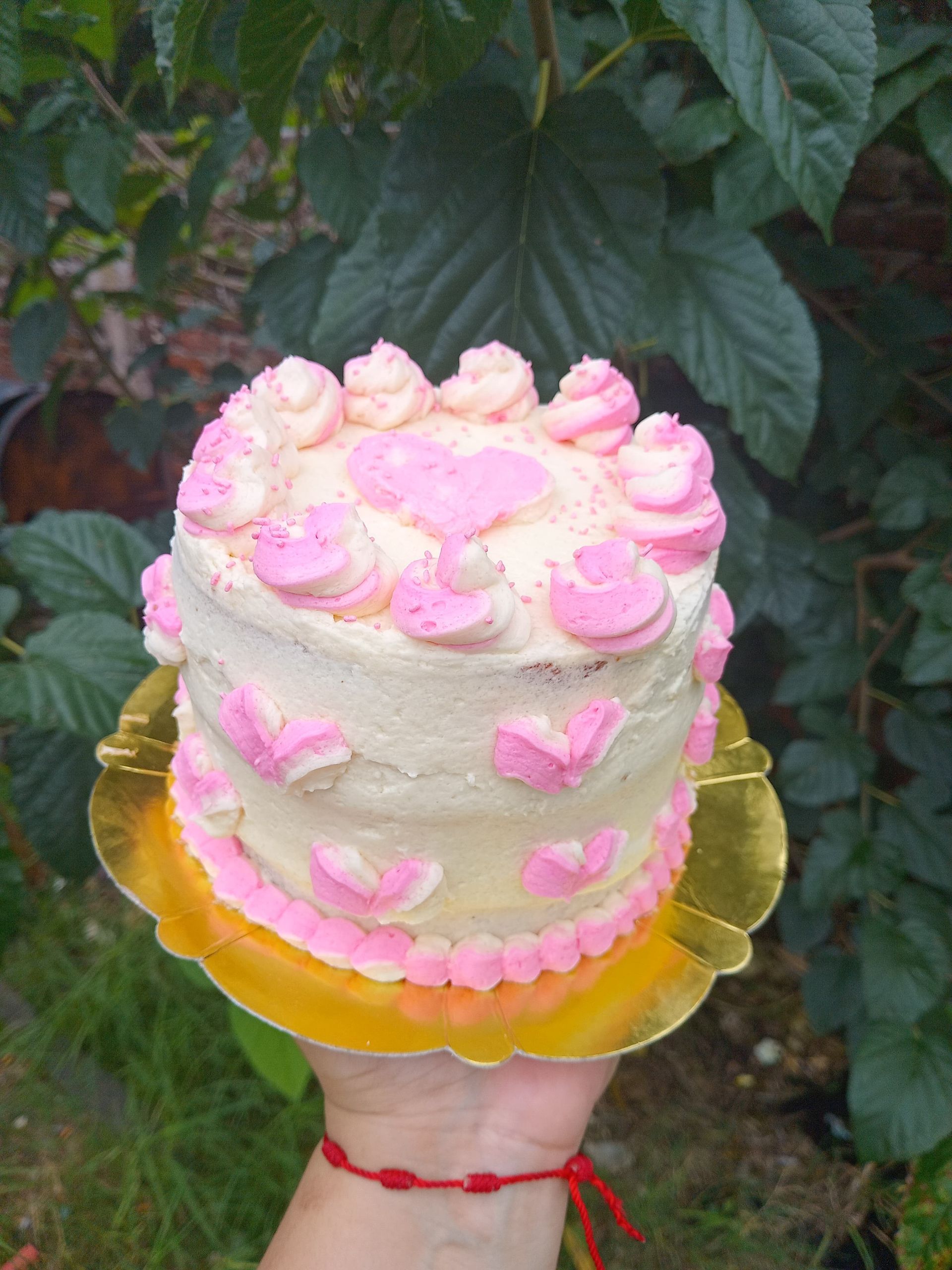 Pequeño pastel decorado con glaseado rosa y blanco, sostenido sobre un fondo verde.