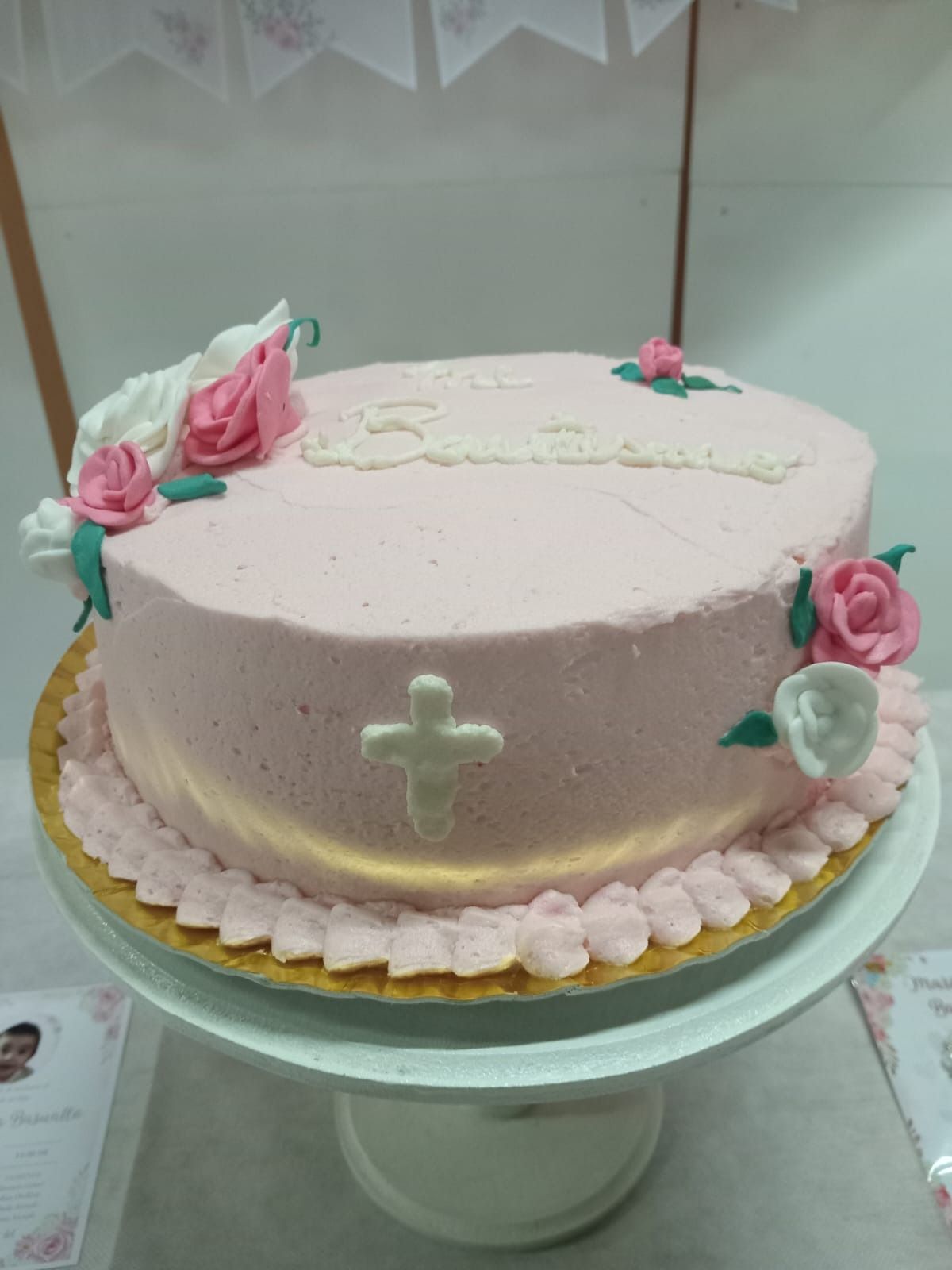 Pastel rosa con adornos florales sobre un pedestal blanco. Una cruz en un lateral y un texto en la parte superior.