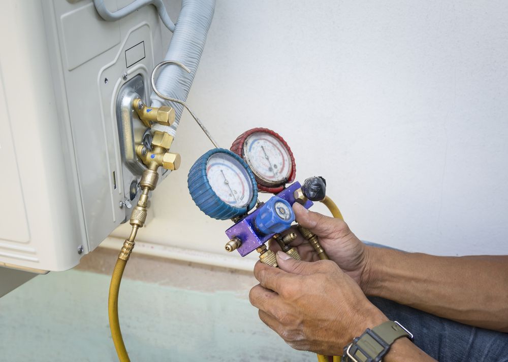 A Person Using Gauges to Service an Ac Unit Outdoors Near a Wall — Vertex Refrigeration & Air Conditioning Pty Ltd In Cannonvale, QLD