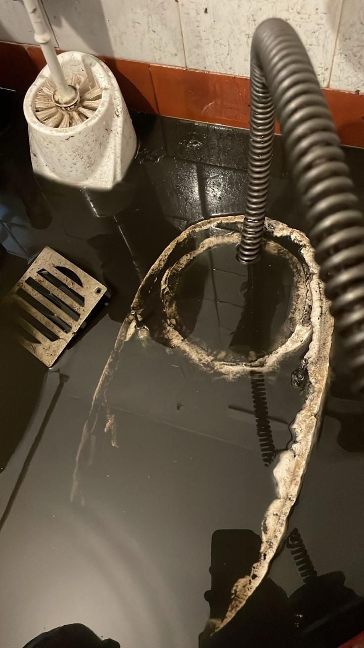 Manguera sucia y rota, y escombros en un suelo mojado junto a un desagüe y un cepillo de limpieza.