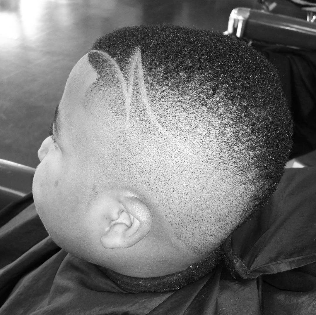 A black and white photo of a child getting his hair cut at a barber shop.