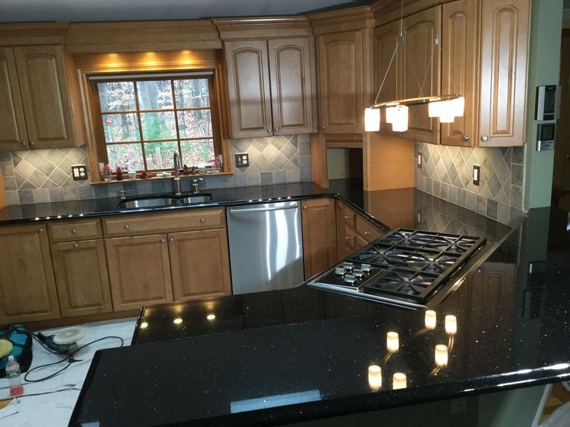 Kitchen with black countertops, light-colored cabinets, and a stainless steel gas stove.  Backsplash is a patterned tile.