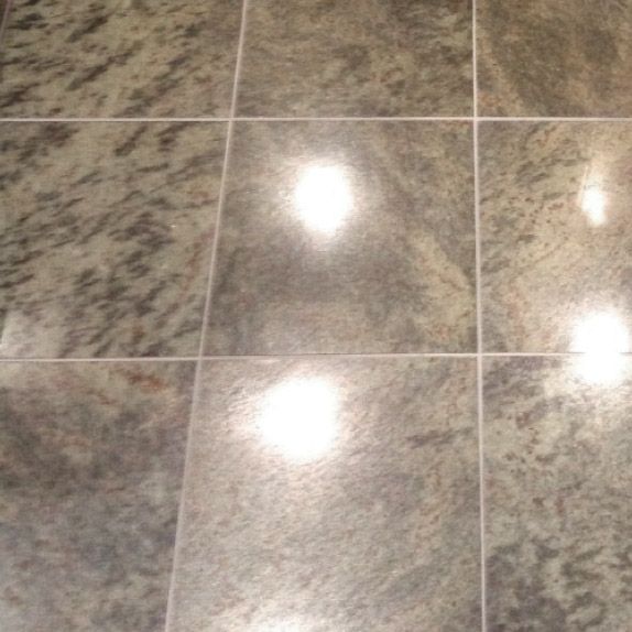 Close-up of nine rectangular tiles of speckled gray stone, with white grout lines separating them. Bright reflections are visible on some tiles.