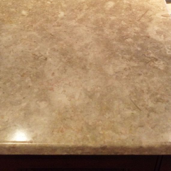 Close-up of a beige and tan marble countertop with veining and a slight shine, likely in a kitchen or bathroom.