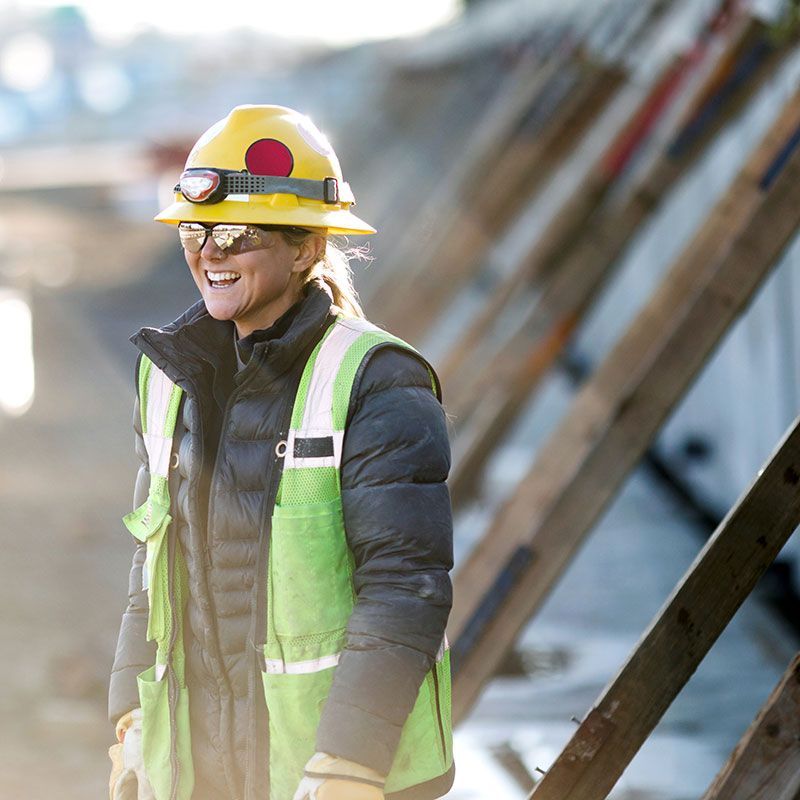A woman wearing a hard hat and safety vest is smiling