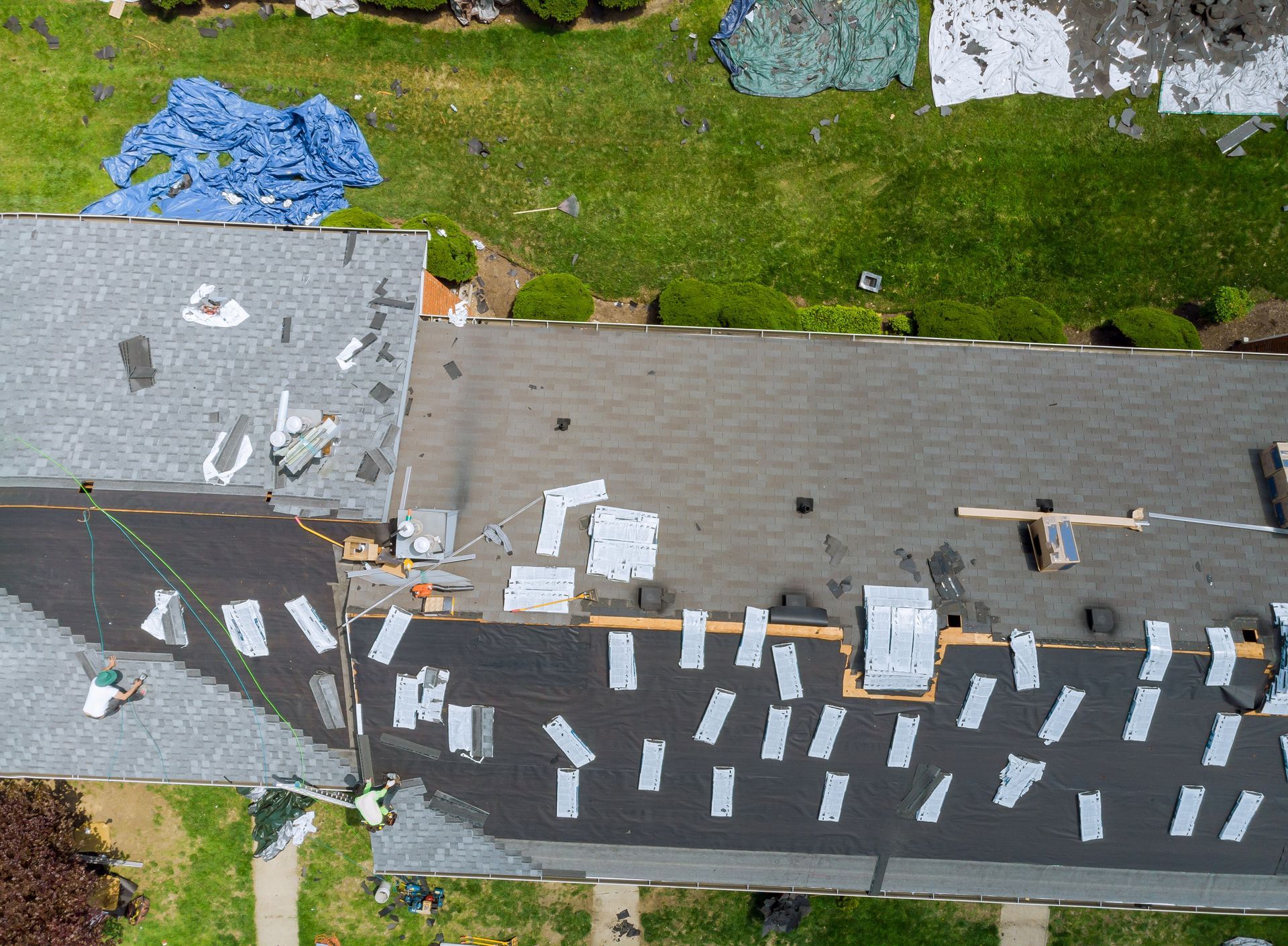Aerial view of a residential roof undergoing repairs with workers, patches of shingles, and protective tarps.