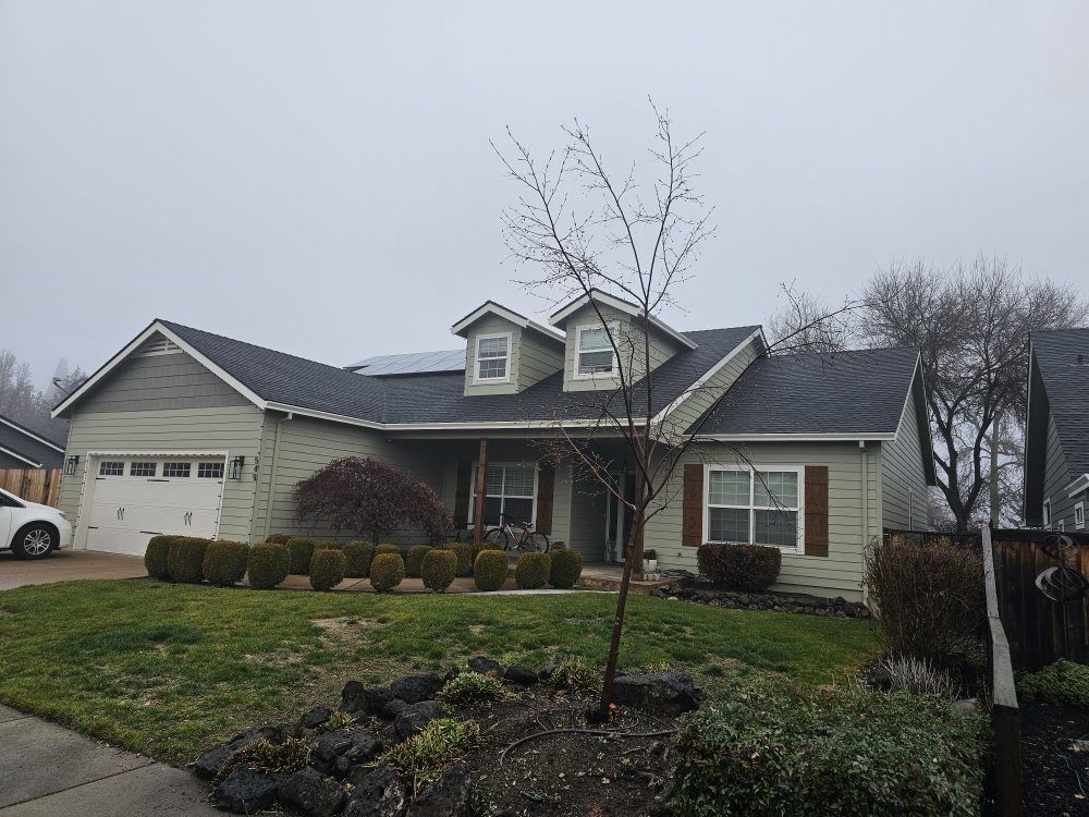 A light green, single-story suburban house with a dark shingle roof, two front-facing dormers, and a manicured front lawn.