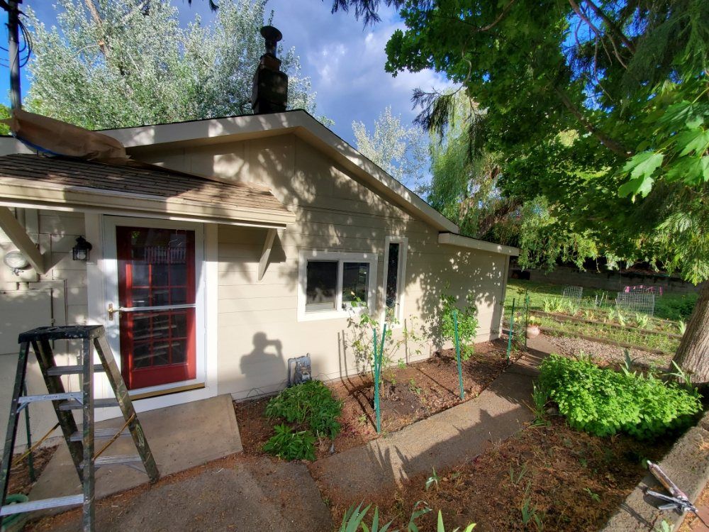 Exterior view of a light-colored house with a red door, a small window, and a ladder leaning against the left side.