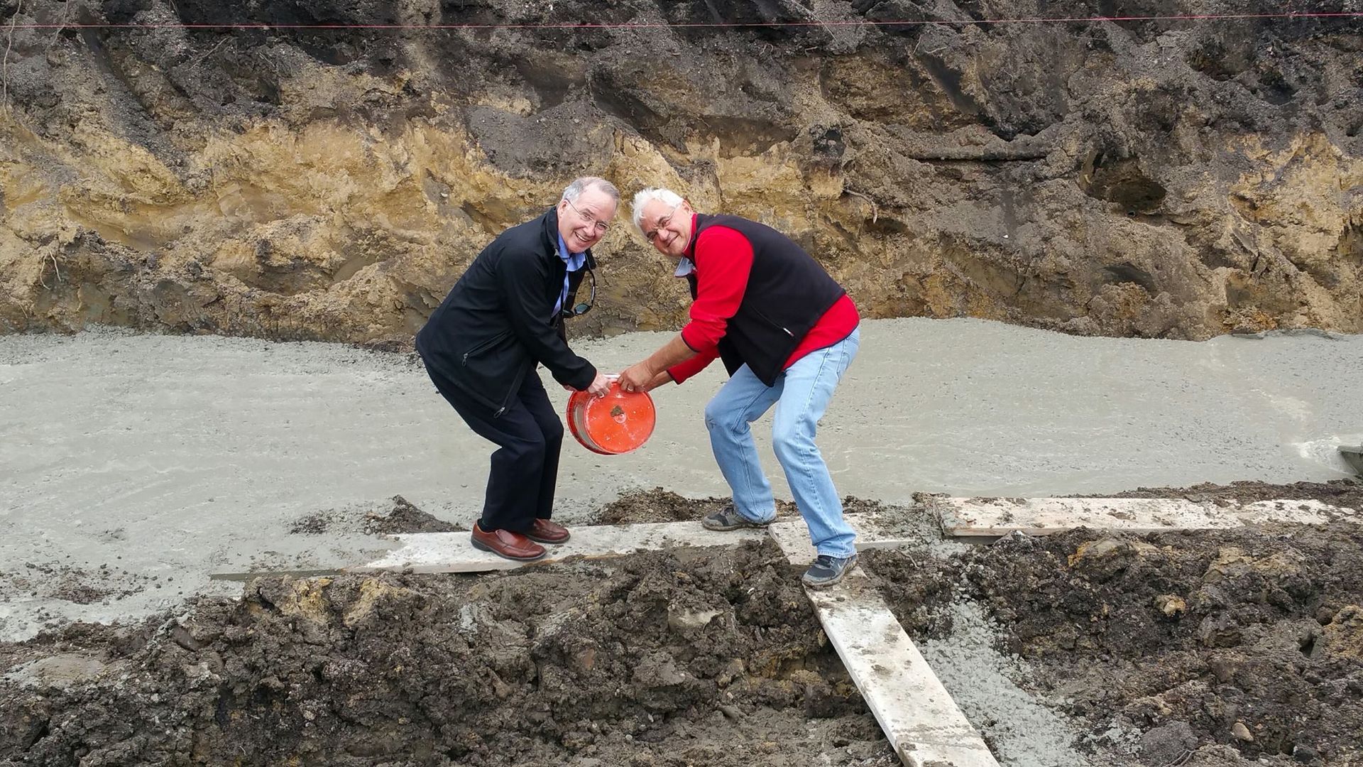 Two men are standing next to each other in the dirt.