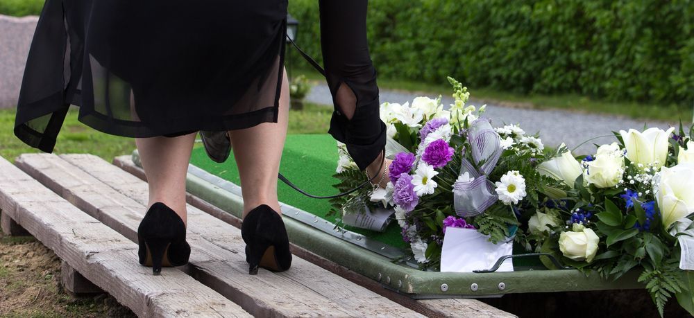 A Woman is Putting Flowers on a Coffin at a Funeral — Mid Coast Funeral and Cremation Service In Port Macquarie, NSW