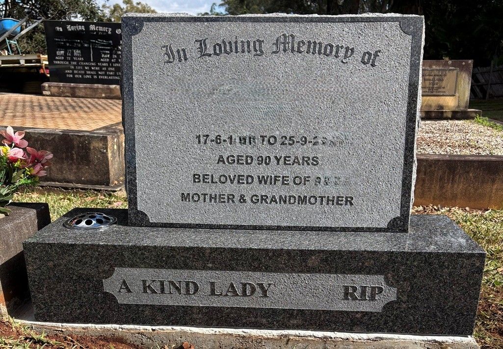 A granite gravestone in a cemetery with a light grey face and dark base, inscribed 