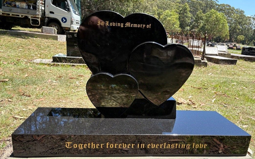 A polished black granite headstone with three heart-shaped markers, engraved with 