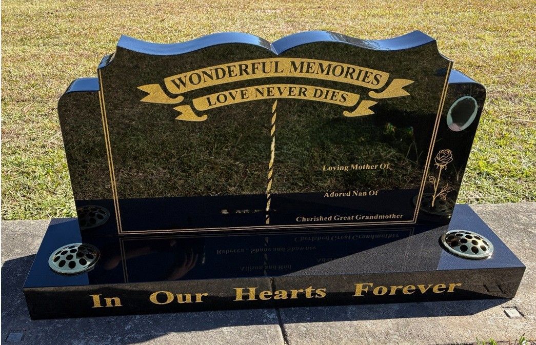 A black granite tombstone with gold lettering reading 