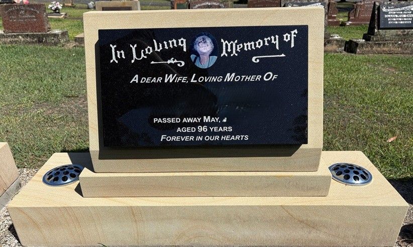 A tan stone headstone with a central black plaque featuring a portrait, inscription, and two metal flower vase inserts — Mid Coast Funeral and Cremation Service In Port Macquarie, NSW