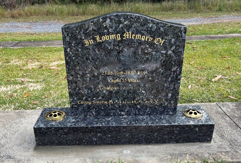 A polished, dark blue-flecked granite headstone with gold lettering, situated on a grass-covered cemetery lot — Mid Coast Funeral and Cremation Service In Port Macquarie, NSW
