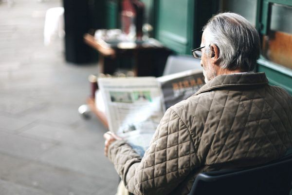 An Older Man is Sitting in a Chair Reading — Mid Coast Funeral and Cremation Service In Port Macquarie, NSW