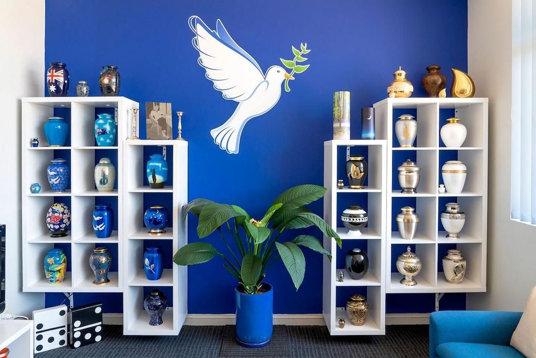 A Room With a Blue Wall and Shelves Filled With Vases — Mid Coast Funeral and Cremation Service In Port Macquarie, NSW