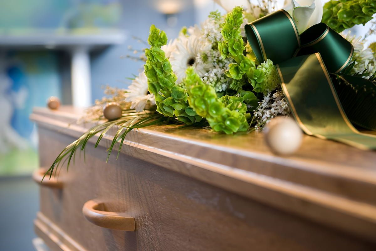 A Wooden Coffin With Flowers and a Green Bow on It — Mid Coast Funeral and Cremation Service In Port Macquarie, NSW