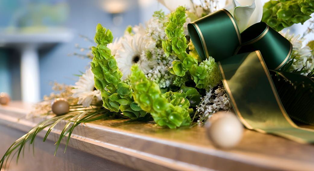A Coffin With Flowers and a Green Bow on It — Mid Coast Funeral and Cremation Service In Port Macquarie, NSW
