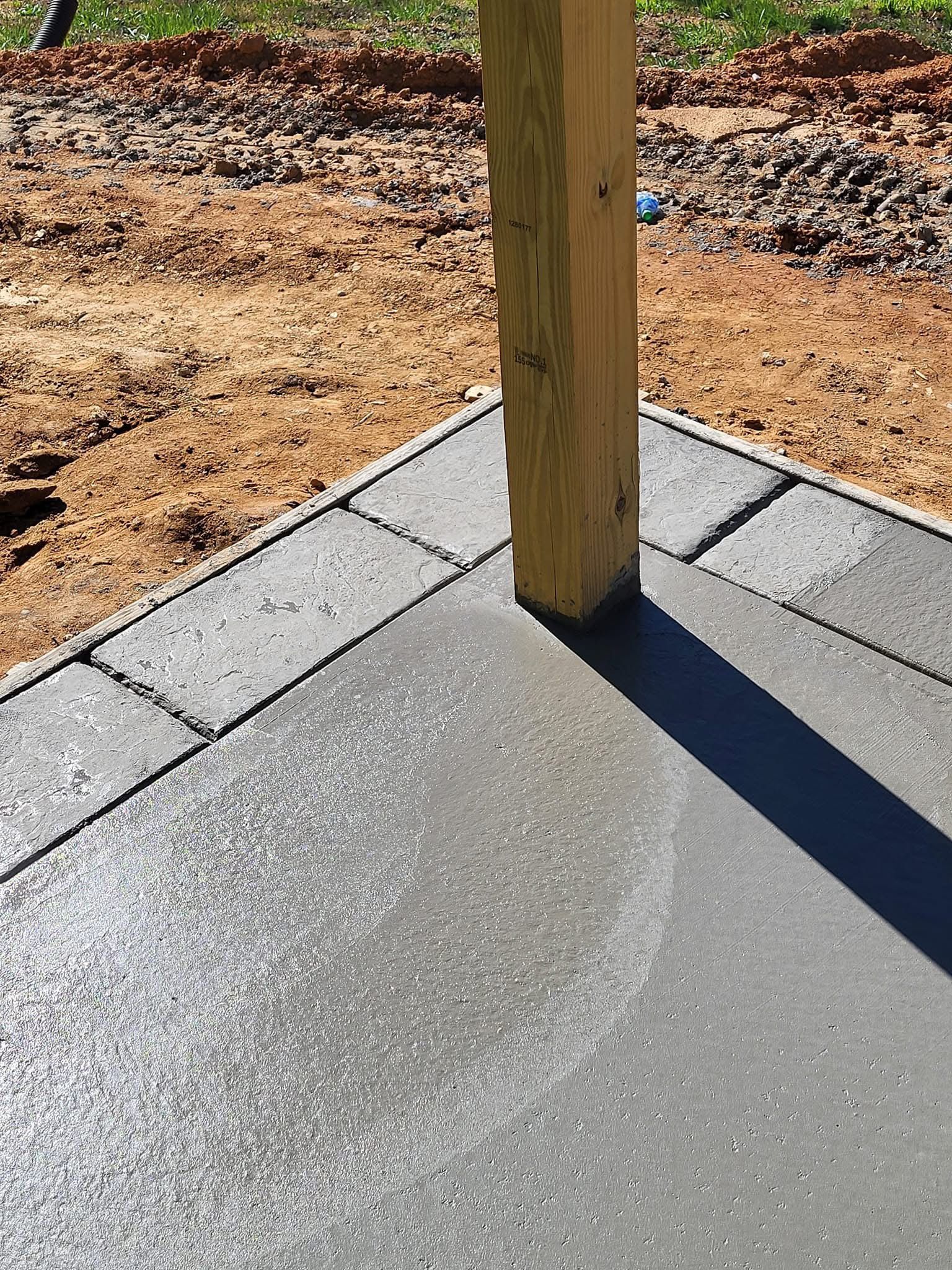 Corner of a concrete patio with a wooden post. Dark gray border and wet, light gray surface.