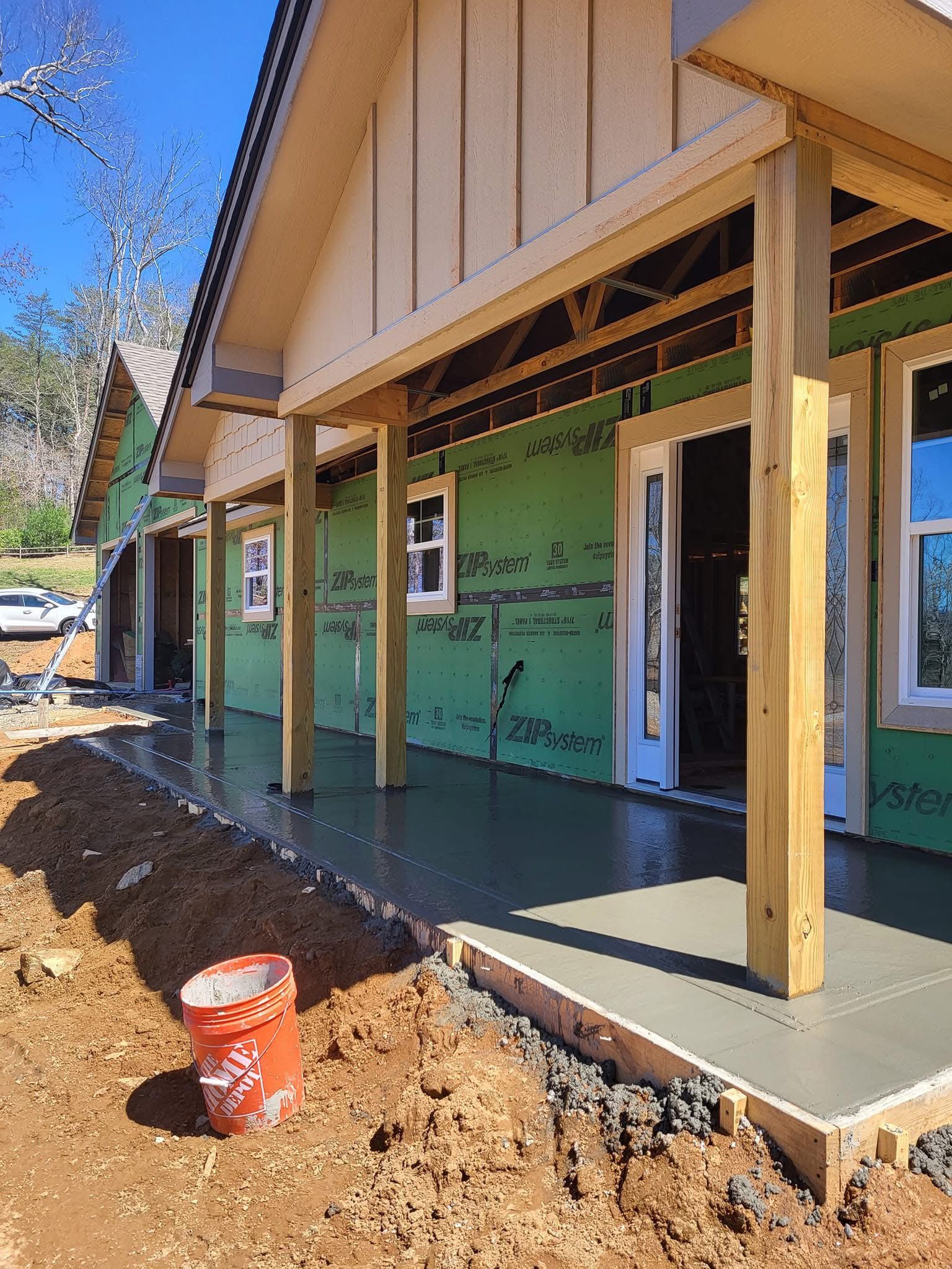 Construction site. New building with porch under construction; concrete walkway, green siding, wood posts.