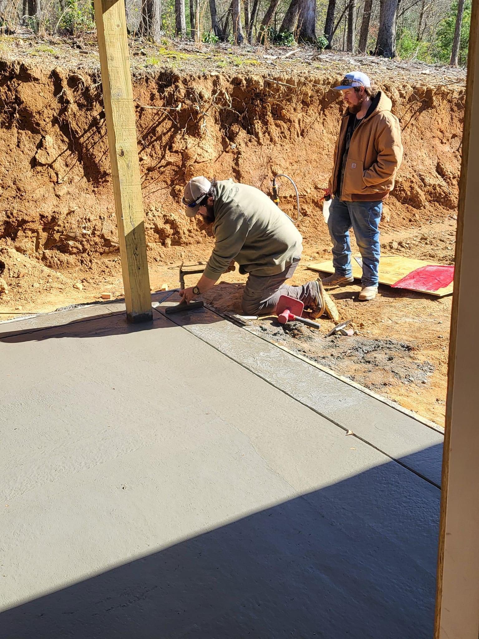 Two construction workers smoothing wet concrete patio.