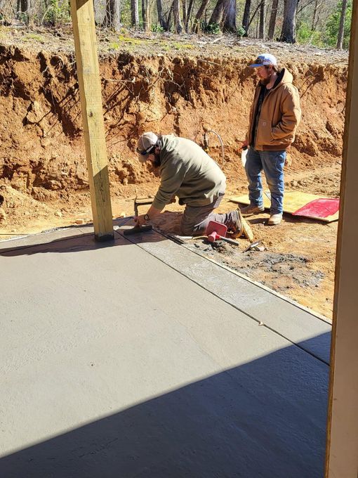 Two construction workers smoothing wet concrete patio.