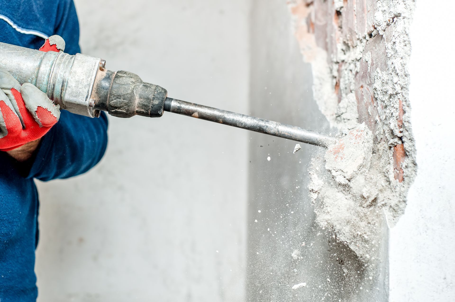 Person using a jackhammer to break through a concrete wall, causing dust.