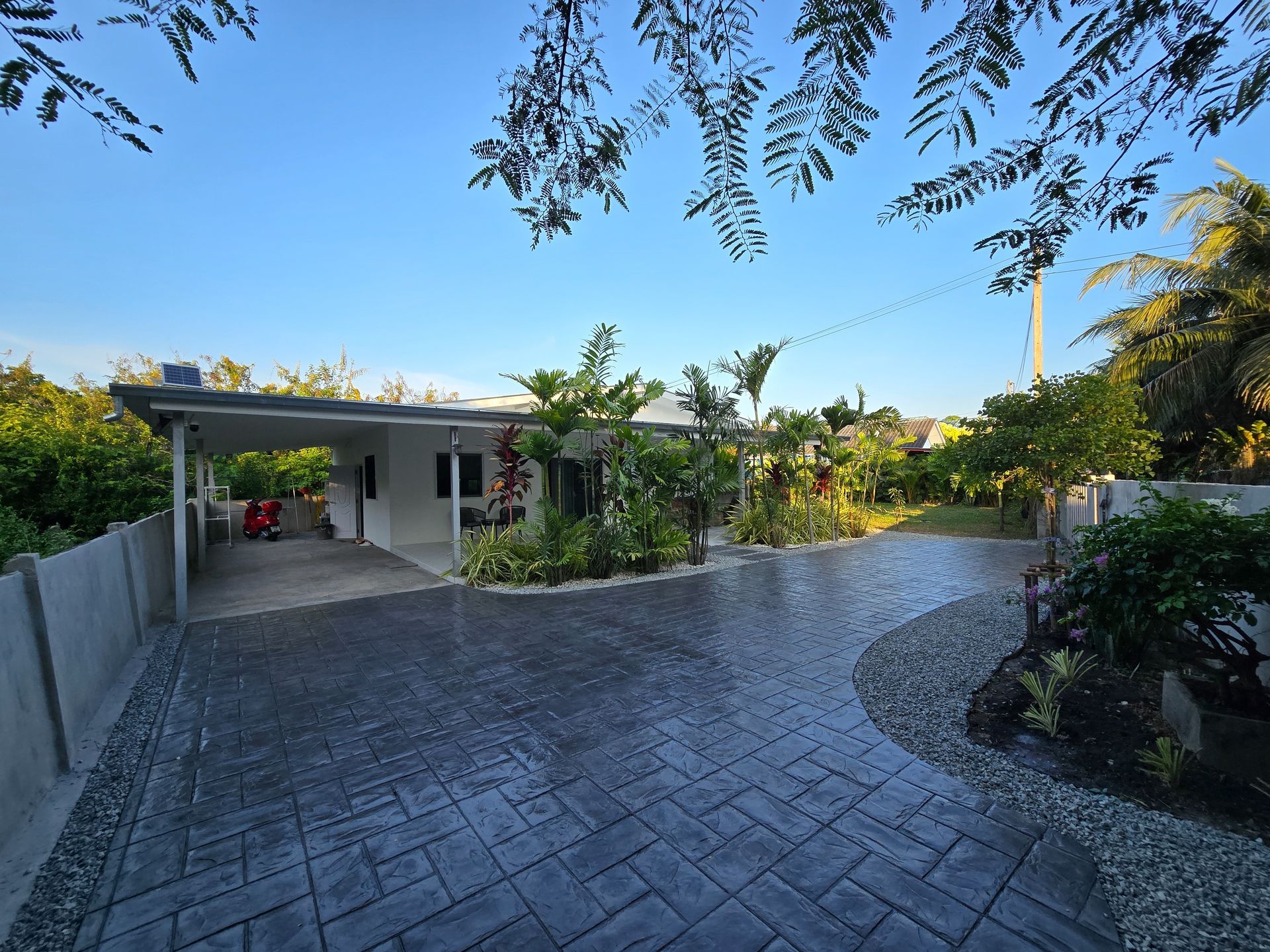 House with paved driveway, carport, and lush landscaping under a blue sky.