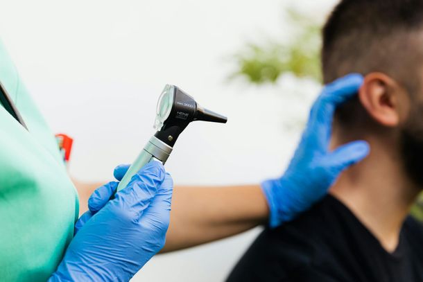 Gloved clinician using an otoscope to examine a patient’s ear