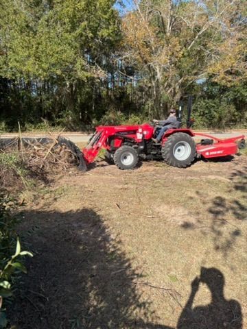 Red tractor with loader and person operating, in wooded area, clearing debris.